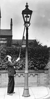 A lamplight at work, holding ignition rod to gas jet in lamp. Circa 1930