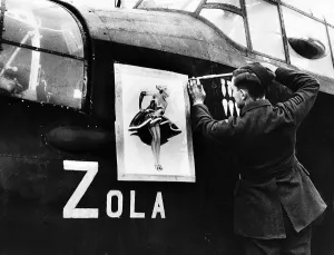 A Lancaster bomber crewman screws on a nose art painting of Zola on to the side of