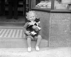 Little Girl With Cat A small child sitting on the steps of a shop holding a cat in