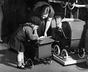 Mother Prints: Little girl putting a doll in a pram at garage helped by her mother