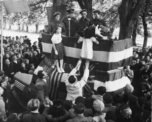 Two little girls being hoisted to the platform to present a bouquet of roses to a French