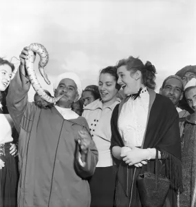 00009 Prints: Local man of North Afric holding up a snake with a group of women gathered around to