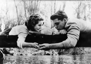 00050 Prints: Love and Romance. Couple holding hands on a log across a stream December 1958