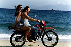 Lynn Wales with Andreas taverna owner on back of motorbike on beach Mykonos