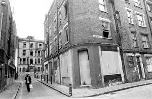 Alley Prints: A man carrying his shopping bag as he walks past delapidated buildings with broken