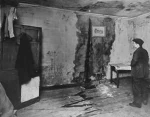 A man inside slum housing in Liverpool inspect a large damp patch on the wall. circa 1935