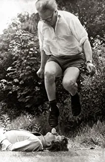 A man leaping over mans face holding an egg in mouth January 1974