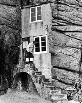 Rocks Prints: A man looks into the window of a tiny house built into the rocks overlooking the sandy