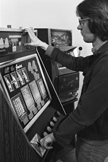 01047 Prints: Man playing a one arm bandit slot machine in a London amusement arcade. 8th January 1975