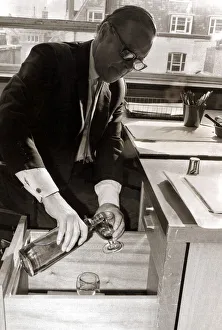 Alcoholic Prints: A man pours himself a drink which he keeps hidden in a filing cabinet in his office