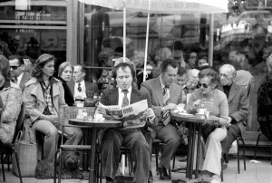 Breakfast Prints: Man reading a newspaper and smoking a cigar as he sits outside in a cafe on the streets
