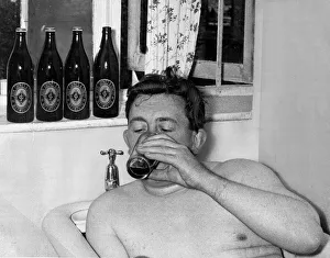 A man relaxes in the bath drinking a bottle of beer September 1955