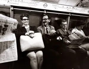 A man smoking a pipe pulls a funny face at his traveling companion. September 1969