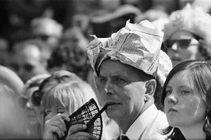 A man smoking a pipe, wearing his newspaper as a hat watches Wimbledon Tennis