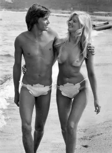 Beachwear Prints: Man and woman stroll arm in arm along the beach. August 1975 P018045