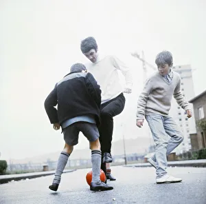 00476 Prints: Manchester United footballer George Best playing football in the street with two young
