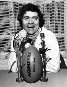 Max Boyce wearing a Doctors cort and stethescoping the English Rose as he indicates