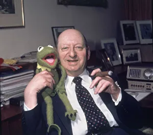 Media Mogul Lew Grade sitting at his desk smoking a cigar while holding Kermit the frog