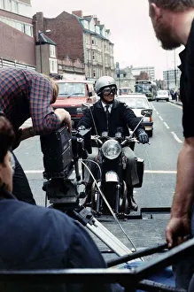 Motorbikes Prints: Michael Elphick actor sitting on motor bike attached rig on the back of lorry filming for