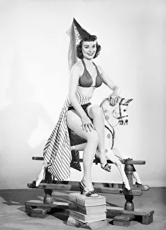 Model dressed as damsel. Riding rocking horse. 1965 E145-005