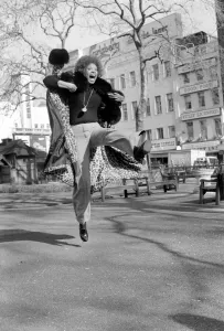 Model Lorne Lesley jumping up in the street February 1975 75-01140-001