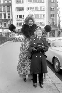 Model Lorne Lesley wearing a long leopard skin coat with fur collar standing behind a