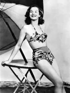 Model wearing a bikini posing by a table underneath an umbrella