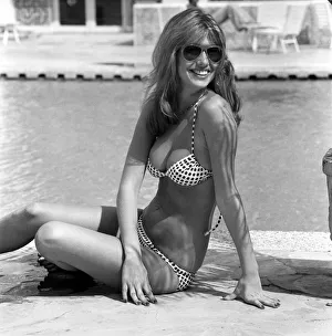 Model wearing a bikini and sunglasses as she sits by the side of a swimming pool in