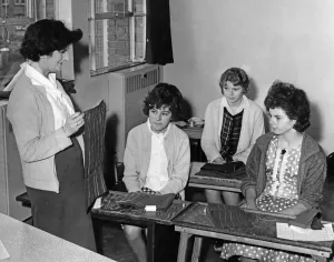 Young Couple Prints: Mrs Lilian Burnard, trainee supervisor for hand sewing, teaching three of the girls in