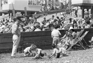 Holidaymaker Prints: Mum enjoys a sandwich and dad looks on as children build sand castles on the beach