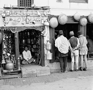 A Nepalese shopkeeper sits in his ironmongers store while shoppers browse his neighbours