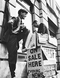 Sellers Prints: Newspaper Seller setting up a stall outside a train station. Circa 1940
