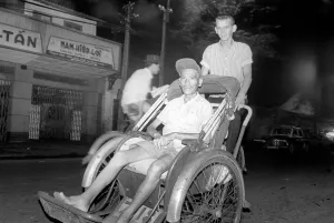 00076 Prints: Night life in Saigon Vietnam. Young man pushes another man in a type of rickshaw