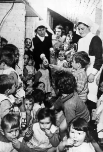 01448 Prints: A nursing sister distributes sweets to these young children while they sit in a wine