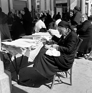 Crafts Prints: Old Greek Woman sewing at her stall waiting for customers in a Cyprus town March