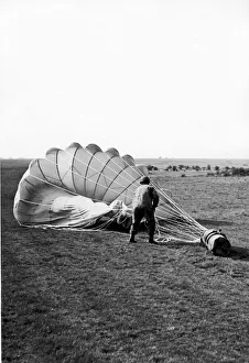 00411 Prints: A paratrooper hauling in the parachute attached to a container which has been dropped