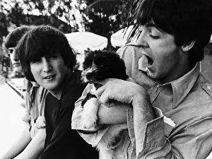 Paul McCartney of The Beatles coddles a puppy watched by John Lennon on the set of Help
