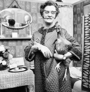 People: Humour: Women: Woman at home holding a chicken in one hand