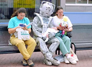 Science And Prints: Person in a robot outfit sits down on a bench next to two women shoppers reading their