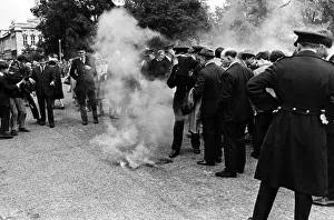 A police officer (centre) prepares to throw his cloak over a smoke bomb hurled as Prince