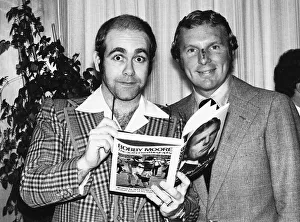 Pop star and chairman of Watford Football Club Elton John helps footballer Bobby Moore