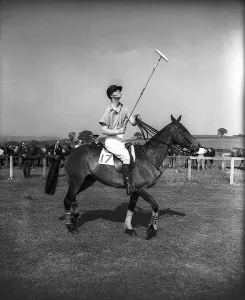 Prince Philip rides along on horseback holding a polo stick during a polo tournament
