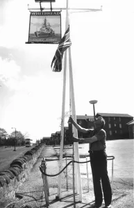 00184 Prints: Publican Fred Howe lowers the Union Jack outside his hostel