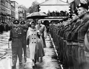 Queen Elizabeth II braves the rain with rain mac and umbrella to inspect a guard of