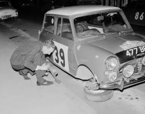 Drivers Prints: Rally driver raymond Baxter repalces the wheel of his Mini car which was removed by some