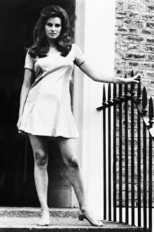 Raquel Welch standing by door in small dress holding onto the side December