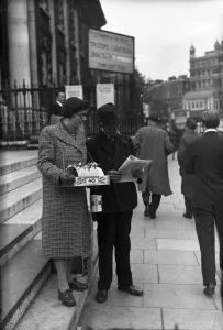 News Prints: Red Cross flag seller in central London catches up on the latest news from Normandy
