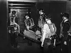Mine Rescue Services carry a miner wearing an oxygen mask on a stretcher into a pit cage