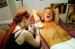 Rod Stewart grimaces in pain 21st June 1999 as tattoo artsit Ronda Hoelzer