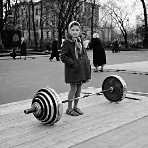 00082 Prints: Russian girl contemplates the dumb bell weights used by the weightlifters in a Moscow